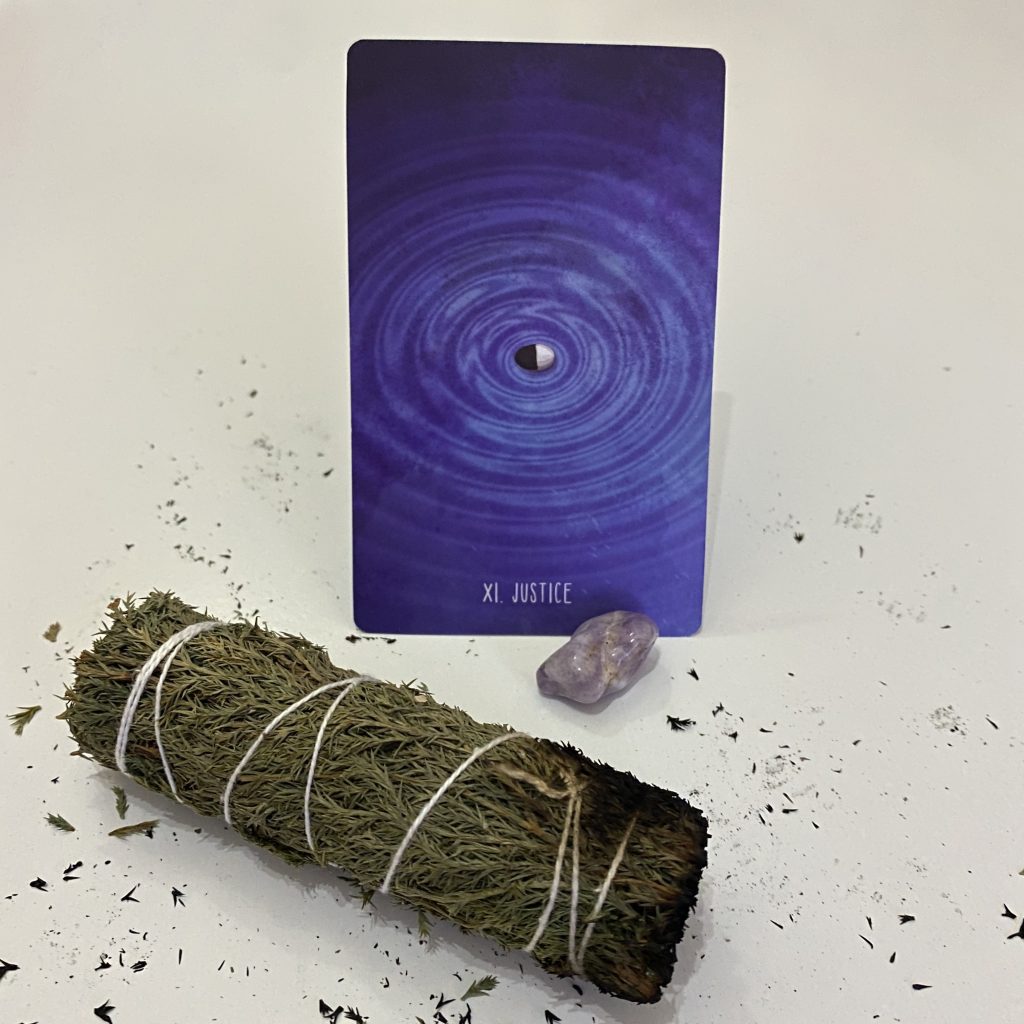 A bundle of sage, a purple Justice tarot card, and an amethyst crystal
