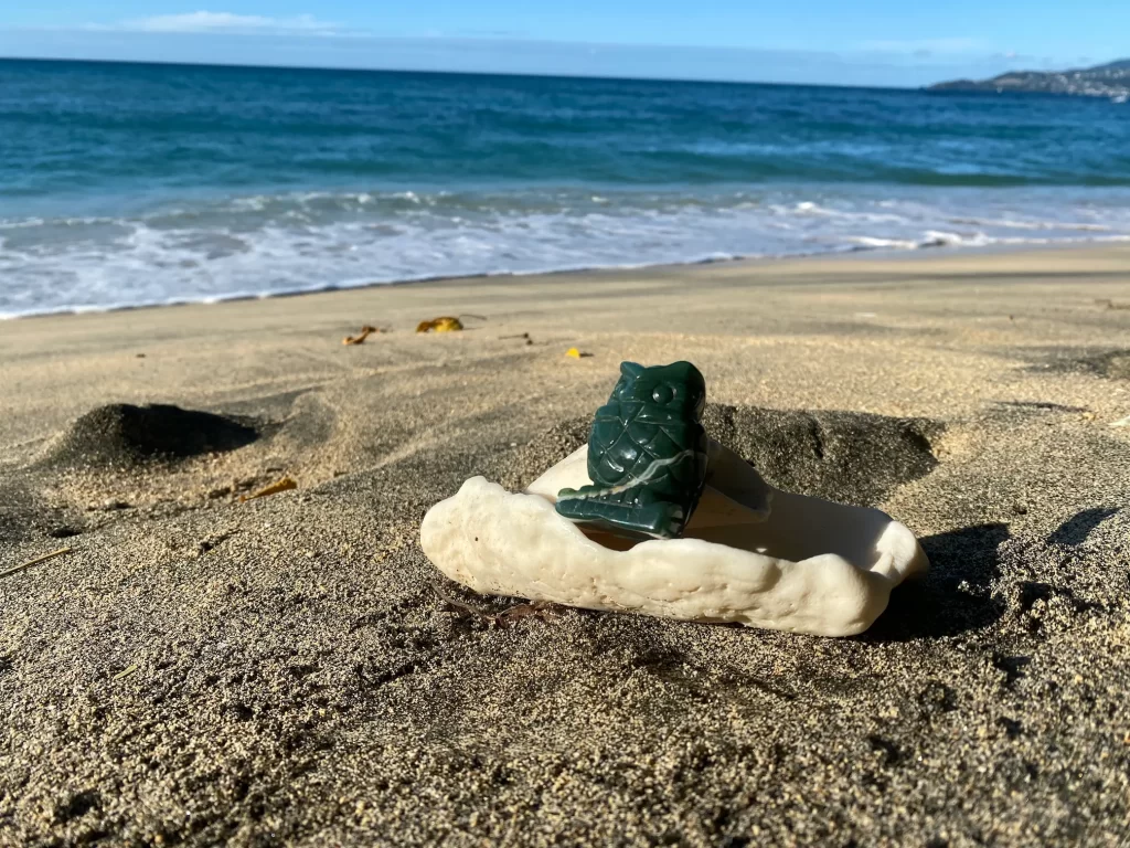 A heart-healing beach scene, with a green owl jade carving sitting on a shell and the ocean waves in the background.